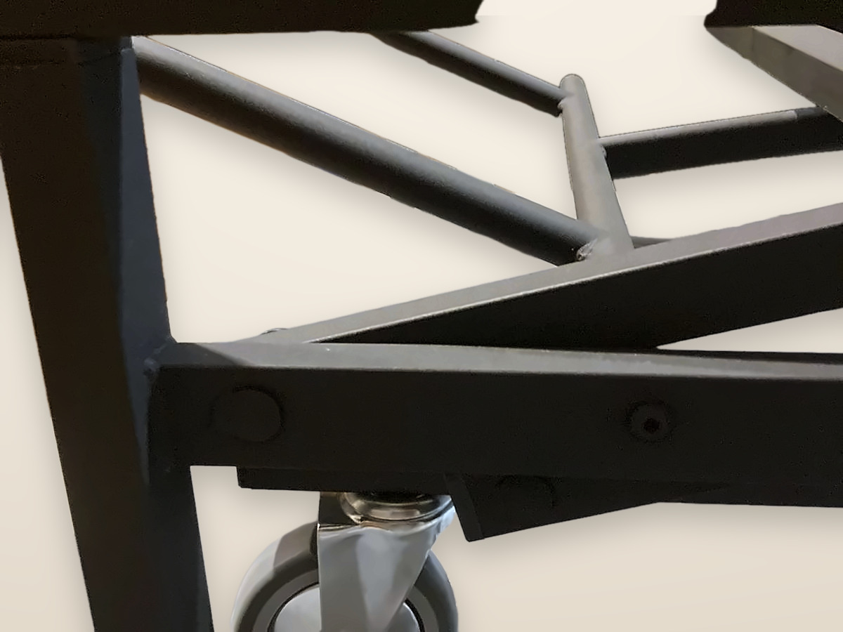 Esquina de la estructura de la cama elevable: perfiles de acero negro con pintura epoxi texturizada, tornillos con tapón y la barra del pedal forrada.