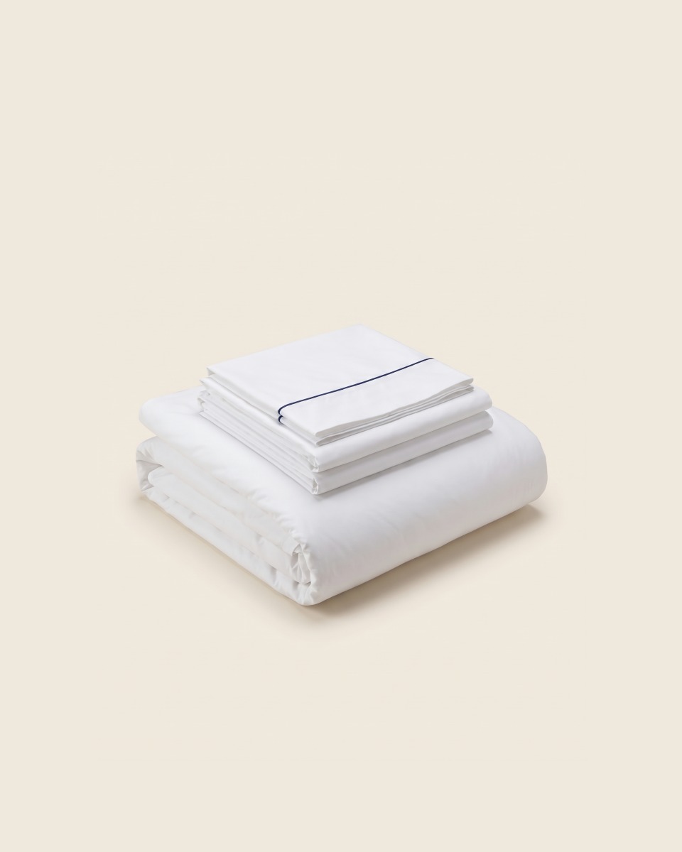 Juego de cama de hotel doblado: sábanas y funda nórdica blancas con un vivo azul en el dobladillo.